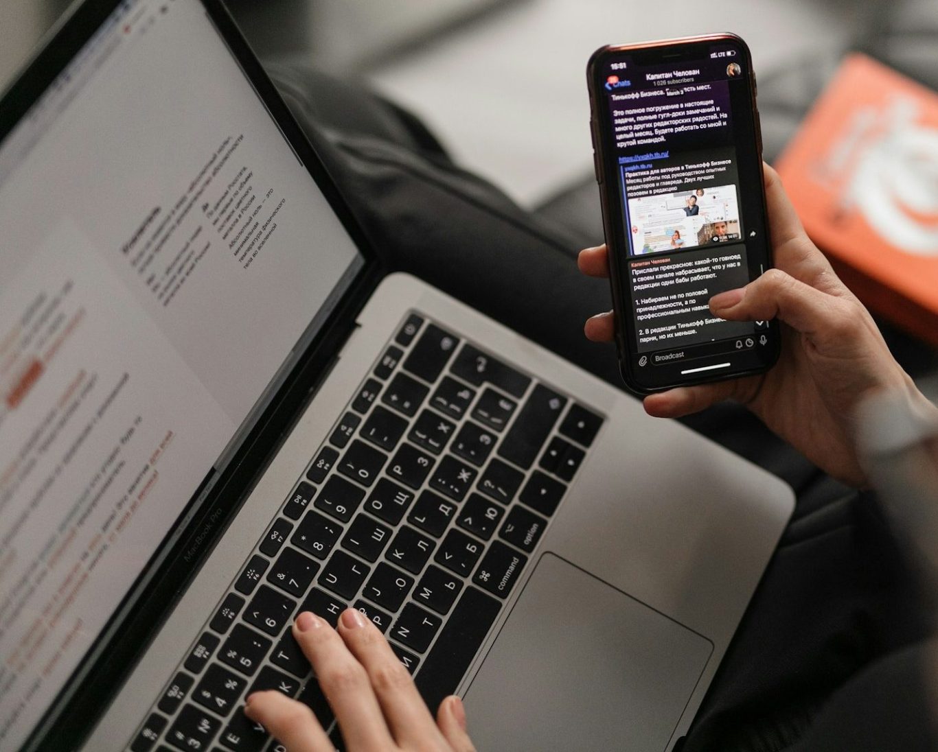 Bild von einer Person, die am Laptop arbeitet und gleichzeitig auf ein Handy schaut.